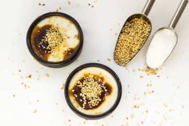 Geleneksel Türk Tarzı Pişmiş Pirinç Pudingi güveçte, kil tatlı kaselerinde, beyaz yüzeyde toz şeker ve doğranmış fındıklı.