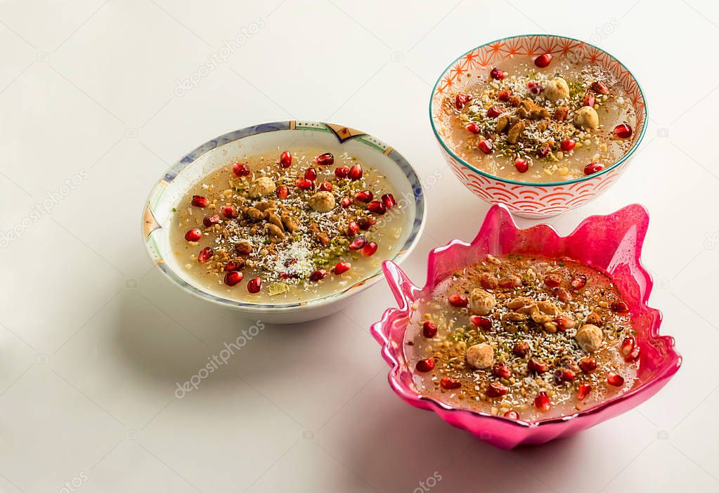 Traditional Turkish Dessert Ashura,Asure or Noah's Ark Puddings with pomegranate seeds in stylish bowls on the white surface.