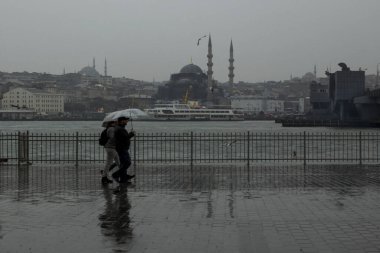 ISTANBUL,TURKEY - JANUARY 5, 2017:A couple is walking with umbrella in front of New Mosque at Eminonu location in the Istanbul.