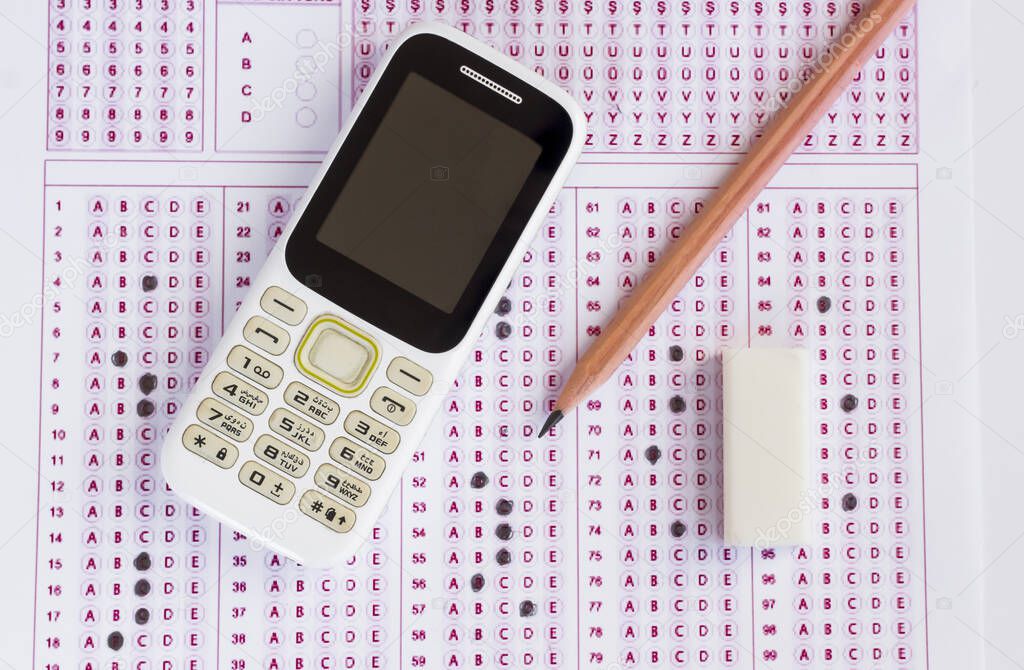 Old cell phone,wooden pencil and rubber on filled exam sheet,conceptual image of education qualifying test exam.