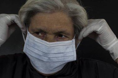 İSTANBUL, TURKEY - 23 Mart 2020: 65 yaşın üzerinde kadın siyah arka planda korunmak için hijyenik yüz maskesi ve eldiven kullanıyor.