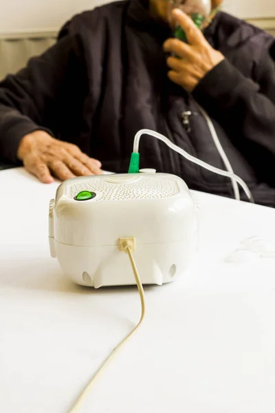 Unknown older person seated and using home type mini air machine \