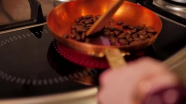 Girl stir coffee beans with a spatula in a copper skillet