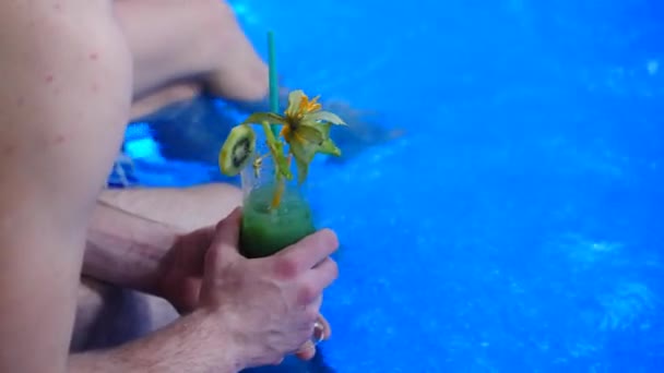 Un homme tenant un cocktail, assis près de la piscine — Video