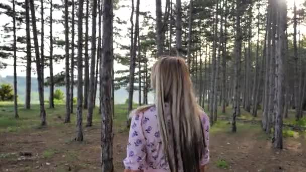 A young blonde girl walks through the pine forest — 비디오