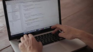 Bilgisayarda çalışan programcı, ahşap bir masada oturuyor.