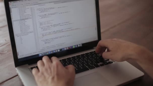 A programozó laptopon dolgozik, egy fa asztalnál ül. — Stock videók