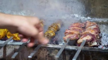 The young man is grilling on the coals the pieces of meat, make kebabs