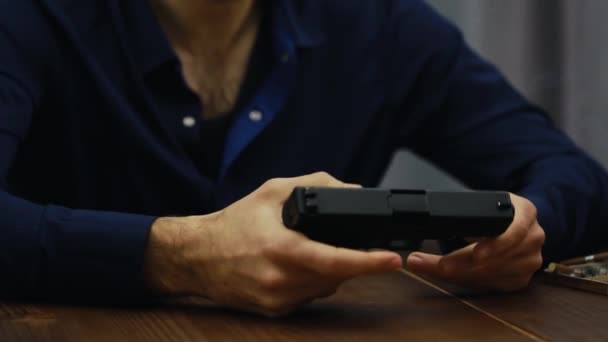 O homem sentado na mesa e segurando uma arma, c vira-lo em suas mãos — Vídeo de Stock