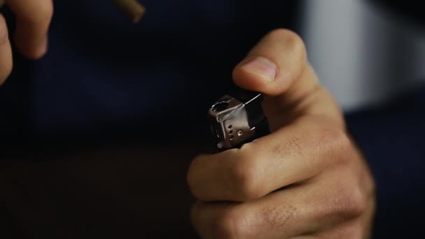 The young man holds a cigar in his hands, lights it with a lighter — Stock Video