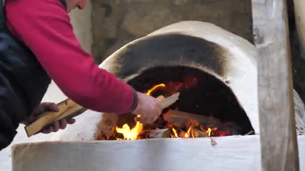 Чоловік розтопив середньовічну плиту, поставивши дрова, щоб пекти хліб . — стокове відео