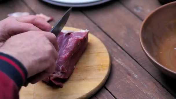 The cook on a wooden plank cuts the meat into pieces to fry it — Stock Video