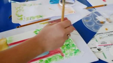 Kız suluboya resimlerle resim yapmayı öğreniyor. Kırmızı bir kemer çizer