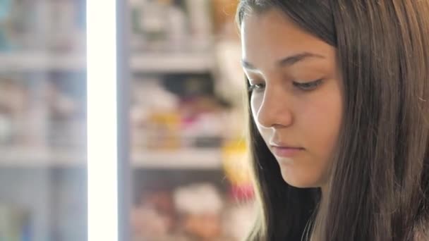 Una joven elige productos en el refrigerador de la tienda. primer plano — Vídeos de Stock