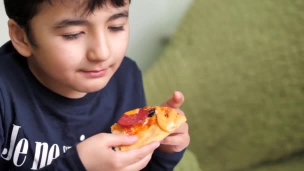 Chlapec s tmavými vlasy jí feferonkovou pizzu a hranolky. zamračené — Stock video
