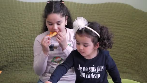 Twee donkerharige krullende meisjes eten pizza en frietjes, dopen het in de saus. — Stockvideo