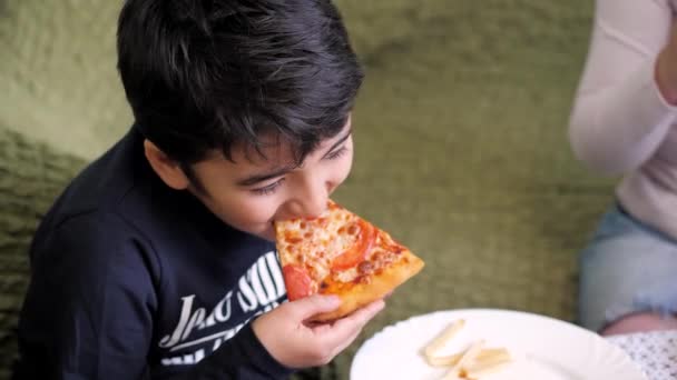 Chłopak z ciemnymi włosami je pizzę i frytki. — Wideo stockowe