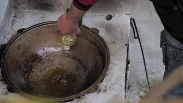 In un calderone caldo di ghisa, il cuoco versa olio per friggere la carne (fegato ) — Video Stock