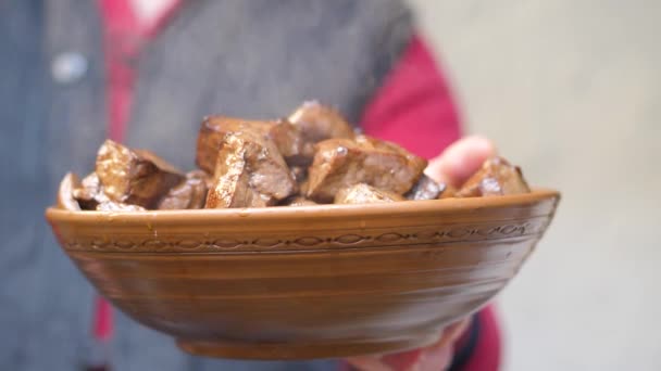 Cook holds in his hands an earthenware dish of fried pieces of beef liver — Stock Video