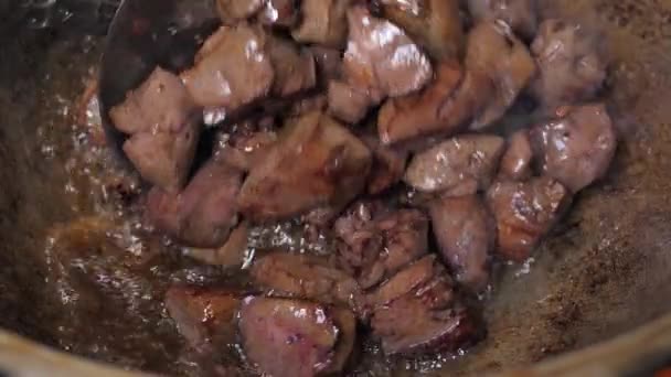 O cozinheiro joga pedaços de carne em uma panela de ferro quente. mistura a carne (fígado ) — Vídeo de Stock
