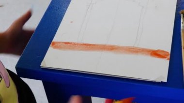 Kız suluboya resimlerle resim yapmayı öğreniyor. Turuncu şeridi çizer
