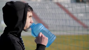 Genç sporcu antrenmandan sonra şişeden su içiyor.