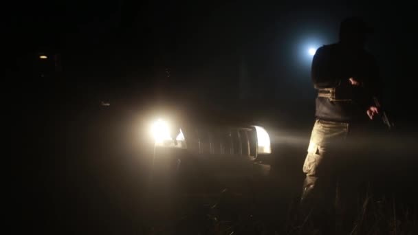 Two armed men stand on the street at night. headlights partially illuminate them — Stockvideo