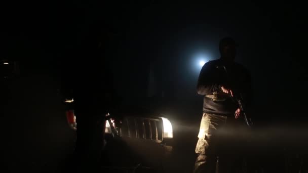 Один вооруженный человек стоит ночью на улице. фары частично освещают его — стоковое видео