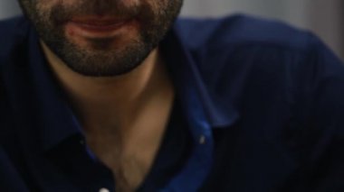 A man with a beard sitting in the room says something and Smoking a cigar