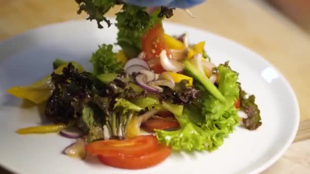 Muž mísí zeleninu a dává salát na bílý talíř — Stock video