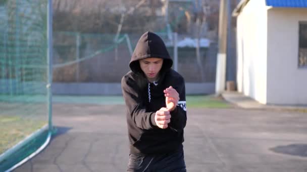 Un joven con una sudadera con capucha hace un calentamiento antes del entrenamiento. acondicionamiento físico — Vídeos de Stock