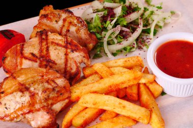 Izgara tavuk parçaları, biber, domates, patates kızartması, ahşap bir tahtanın üstünde soğan.