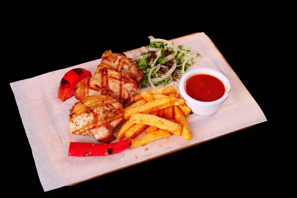 Izgara tavuk parçaları, biber, domates, patates kızartması, ahşap bir tahtanın üstünde soğan.