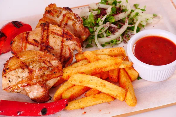Izgara tavuk parçaları, biber, domates, patates kızartması, ahşap bir tahtanın üstünde soğan.