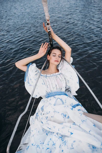 Beautiful woman lies on yacht in a gentle light dress. Beautiful model lies on yacht and plivites by sea