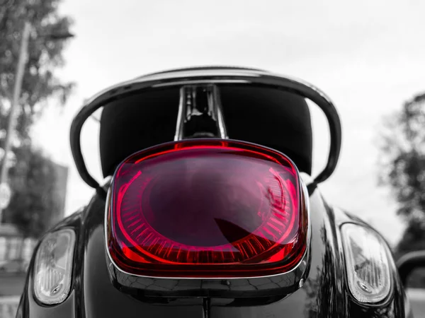 A close up of the rear moped ligth. Red moped light on a black and white picture.