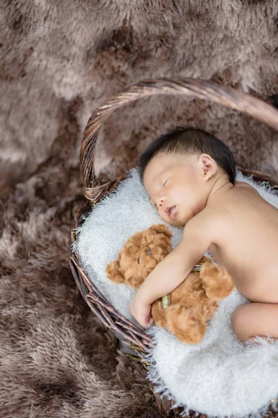 Pequeno bebê dormindo abraçando um urso na cesta — Fotografia de Stock