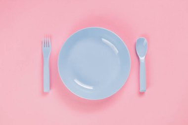 Blue plastic plate with spoon and fork on pink background