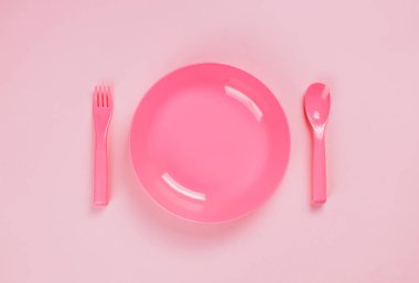 Pink plastic plate with spoon and fork on pink background