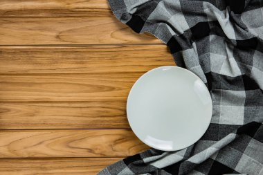 A white plate rests on a Black checkered tablecloth on wooden ta