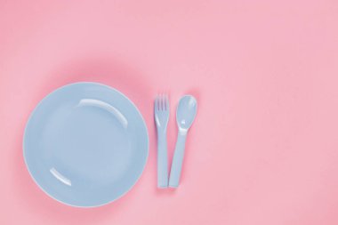 Blue plastic plate with spoon and fork on pink background