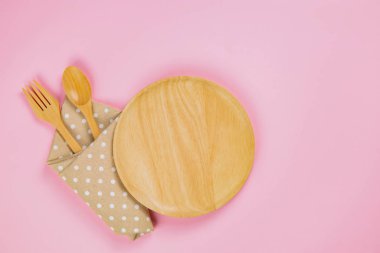 wood plate with spoon, fork and polka dot cloth napkin on pink b