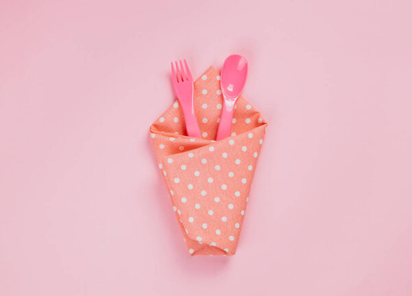 Plastic spoon, fork and pink polka dot cloth napkin on pink back
