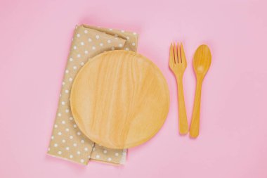 wood plate with spoon, fork and polka dot cloth napkin on pink b