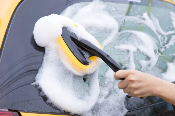 Limpeza do pára-brisas de um carro com espuma de esponja amarela . — Fotografia de Stock