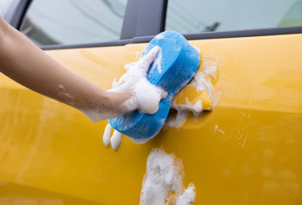 Primer plano de la mano con esponja azul lavado coche amarillo — Foto de Stock