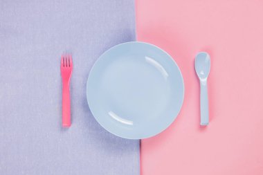 Blue plastic plate with spoon and fork on pink background