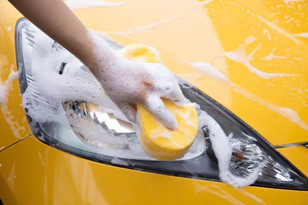 Esponja lavadora limpieza faros de un coche amarillo — Foto de Stock