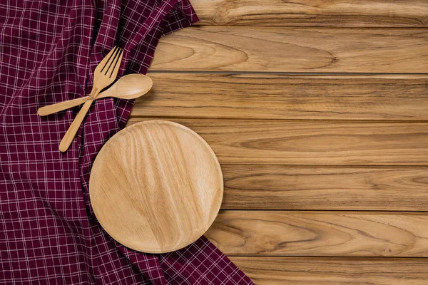 A wood plate rests on checkered tablecloth. There are spoon and — Stock Photo, Image