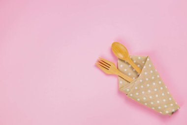 wood spoon, fork and polka dot cloth napkin on pink background